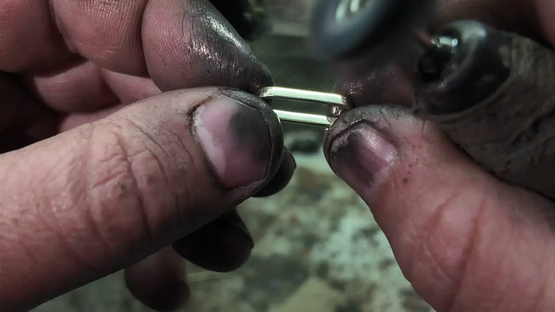 Hands hold a rectangular jewelry component beside a rotary finishing tool.